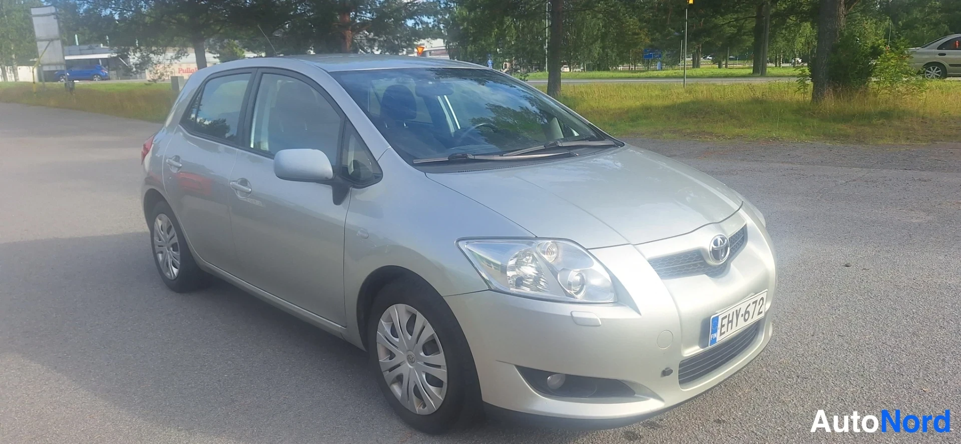 Etuviisto, nokka oikealle: Hopeanvärinen hatchback kolmneselakulmassa edestä oikealta; etusäleikö ja Toyota-merkki näkyvät, rekisterikilpi.
