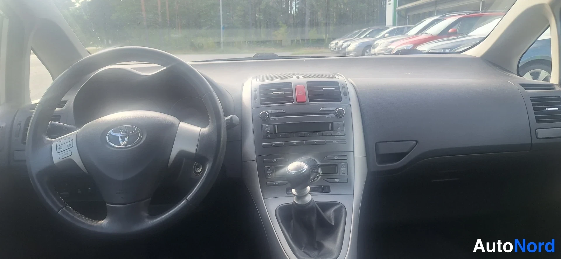 Muu: Toyota Aurisin sisätilat ohjauspyörän ja manuaalivaihteiston osalta, kojelauta ja keskikonsoli näkyvissä.