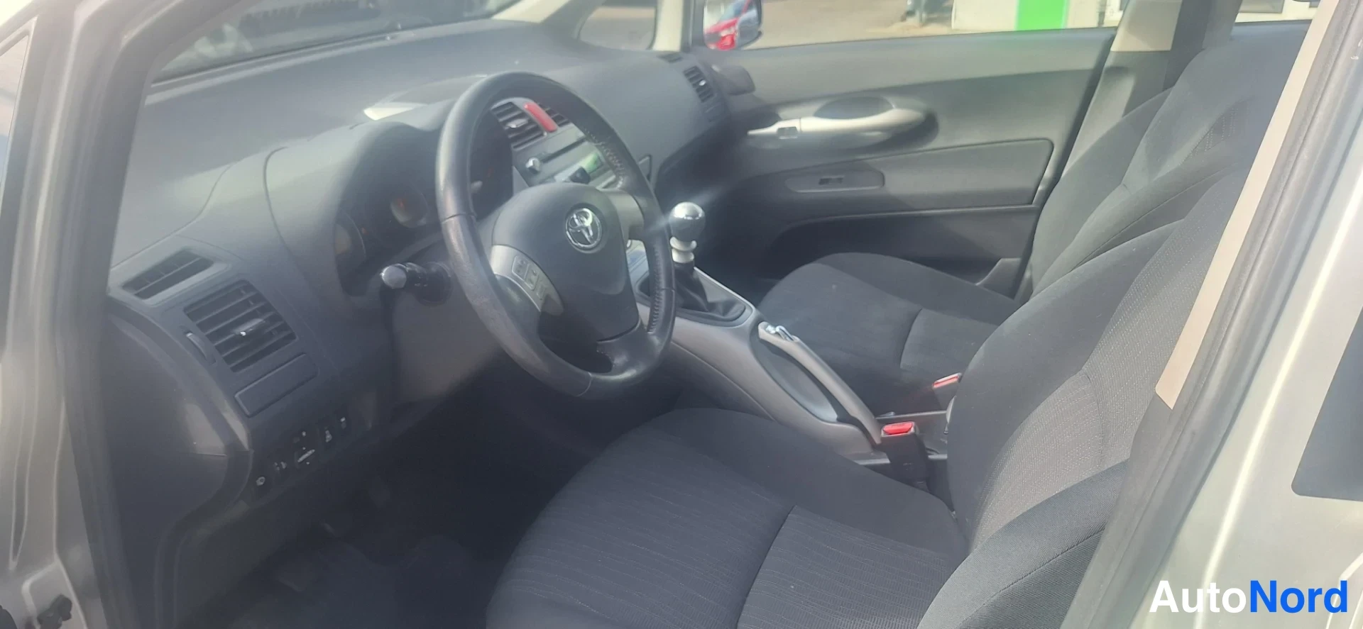 Muu: Toyota Aurisin etusija ohjaamosta, etuistuimet ja manuaalivaihtajanupi näkyvissä.