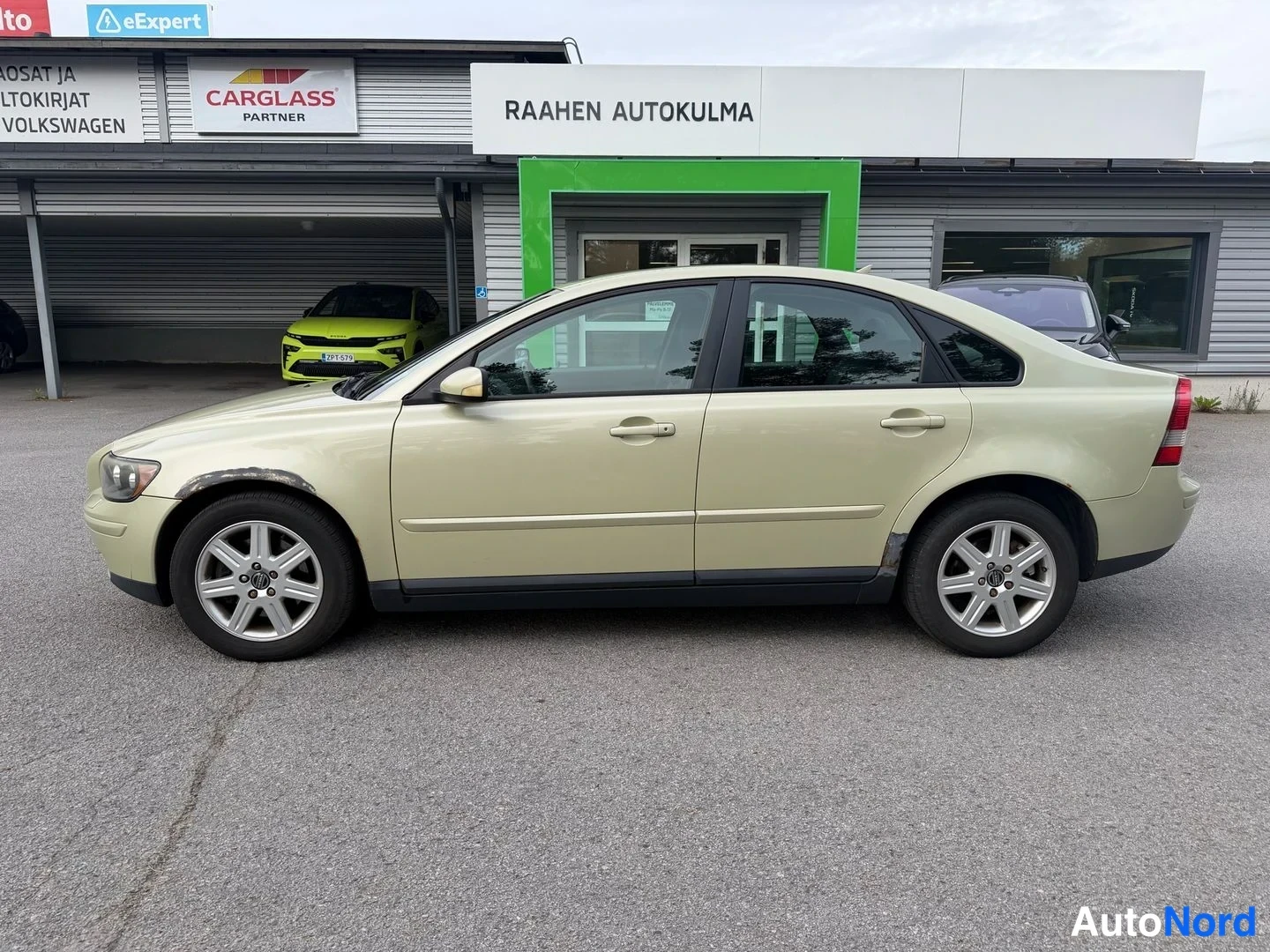 Sivulta: Vaaleanbeige sedan sivulta oikealta kuvattuna, kokonainen kylki ja neljä ovea näkyvissä.