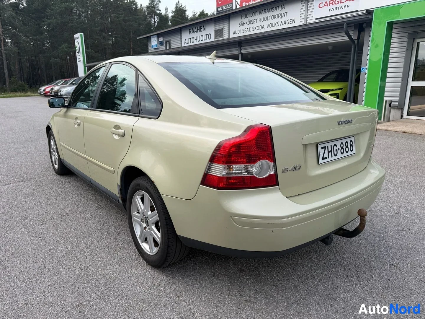 Takaviisto: Vaaleanbeige Volvo S40 takaapäin vasemmalta kolmanneskulmasta, perävaunukoukku ja rekisteritunnus näkyvissä.