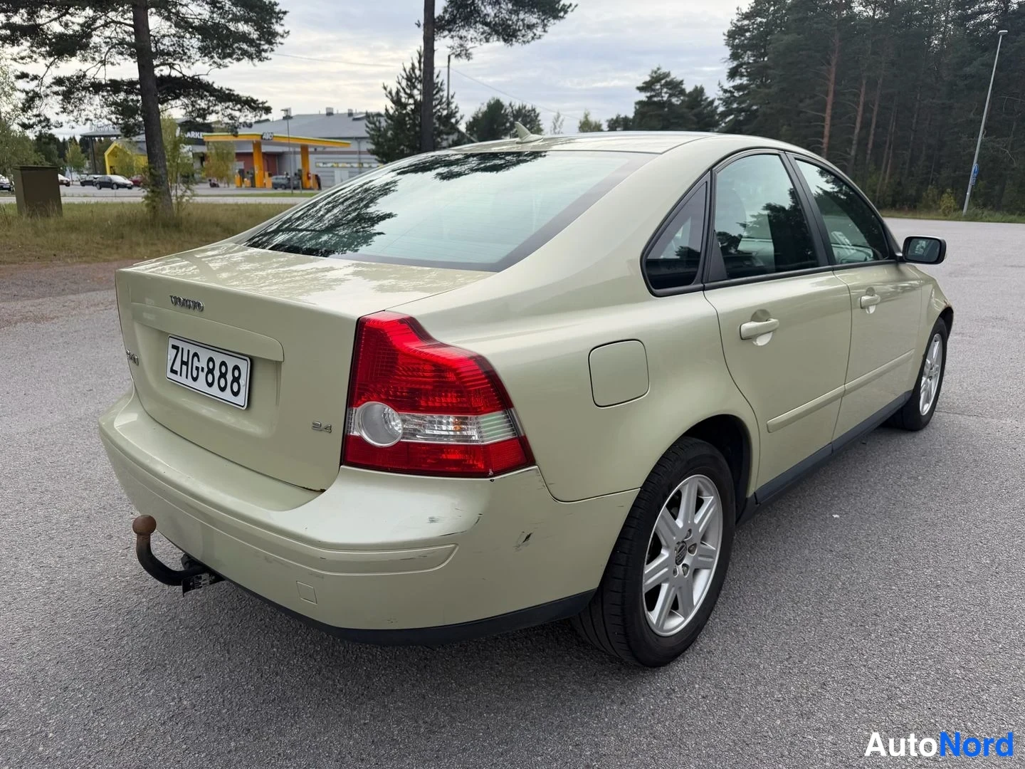 Takaviisto: Vaaleanbeige sedan takaapäin vasemmalta kolmanneskulmasta, perävaunukoukku näkyvissä, rekisteritunnus.