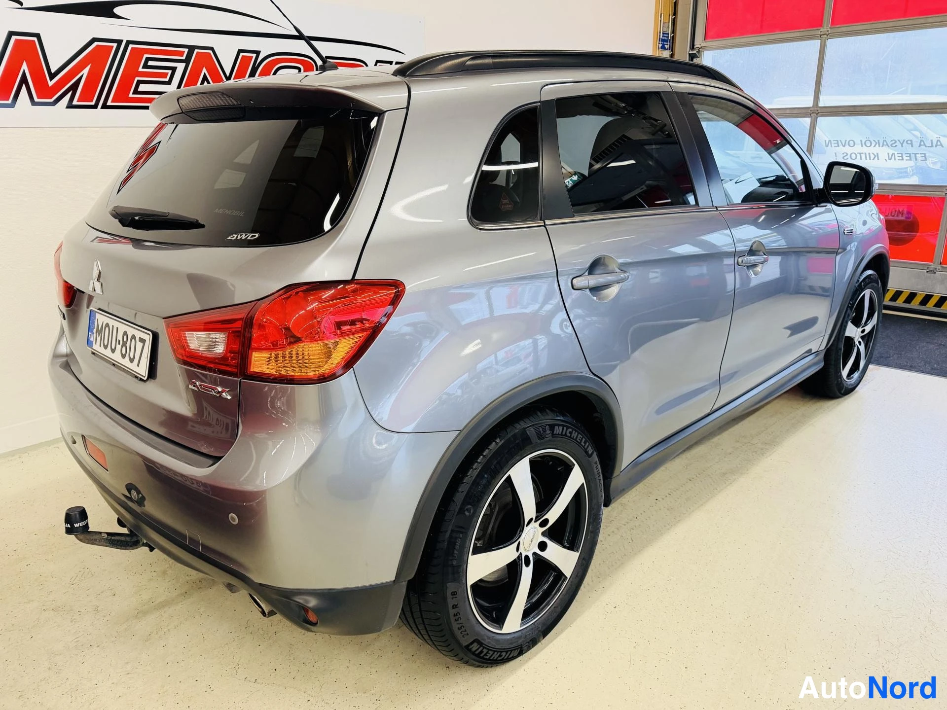 Takaviisto: Hopeisen Mitsubishi-hatchbackin takakolmasosan näkymä vasemmalta; näkyvät takavalot, -rekari, spoileri, kattokaiteet ja mustat vanteet.