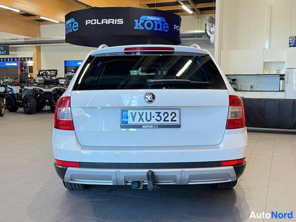 Takaa: Straight rear view of a white estate car: tail lamps, central logo on the boot lid, rear windscreen with wiper, parking sensors on the bumper, tow ball mounted