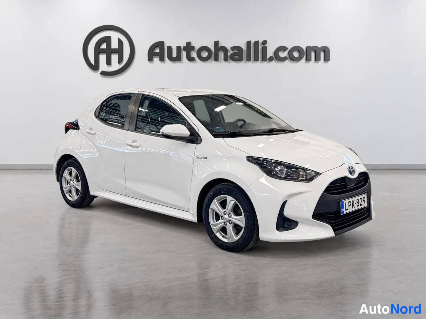 Etuviisto, nokka oikealle: Valkoinen Toyota Yaris -henkilöauto kuvattu kolmivartalokulmassa edestä oikealta autohallin sisätiloissa.