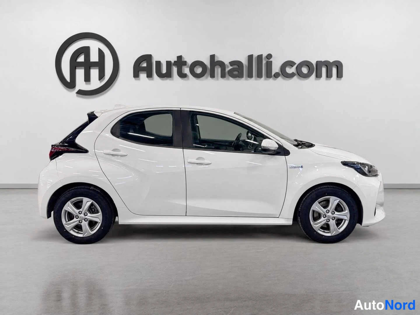 Sivulta: Valkoisen Toyota Yaris -henkilöauton sivunäkymä oikealta puolelta autohallin sisätiloissa.