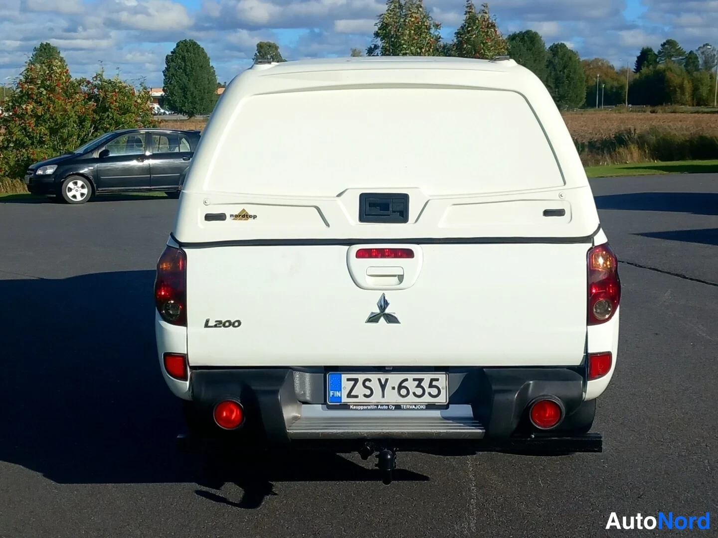 Takaa: Mitsubishi L200 -lavamäärä autotallikuvassa takaa päin: valkoinen hardtop-kate, L200-merkintä ja rekisterikilpi.