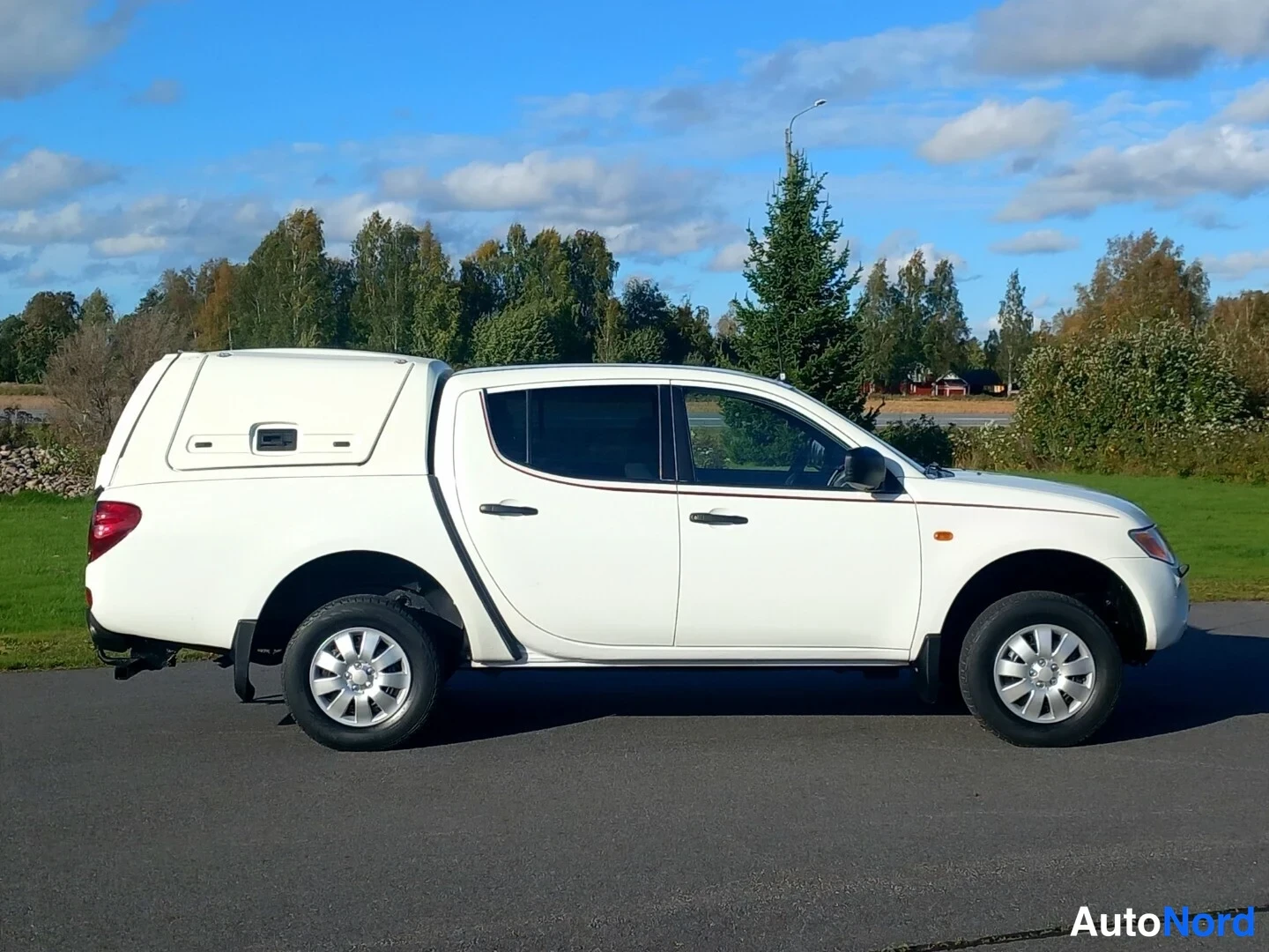 Sivulta: Valkoinen avolava-auto sivuprofiilissa vasemmalta oikealle; lavakate ja mustat ovienkahvat näkyvät.