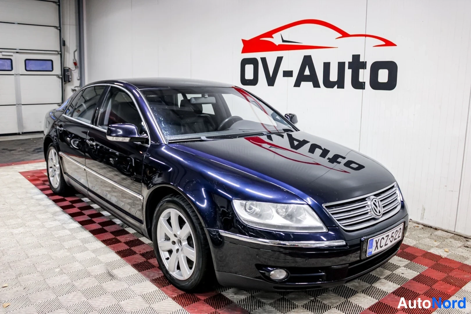 Etuviisto, nokka oikealle: Volkswagen Phaeton -sedanin etukulma vasemmalta kuvattuna sisätiloissa, tummansininen