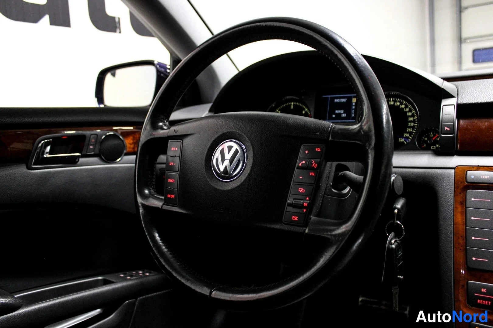 Muu: Lähikuva VW-ohjauspyörästä monitoiminapeineen, taustalla mittaristo ja puukoristeinen kojelauta.