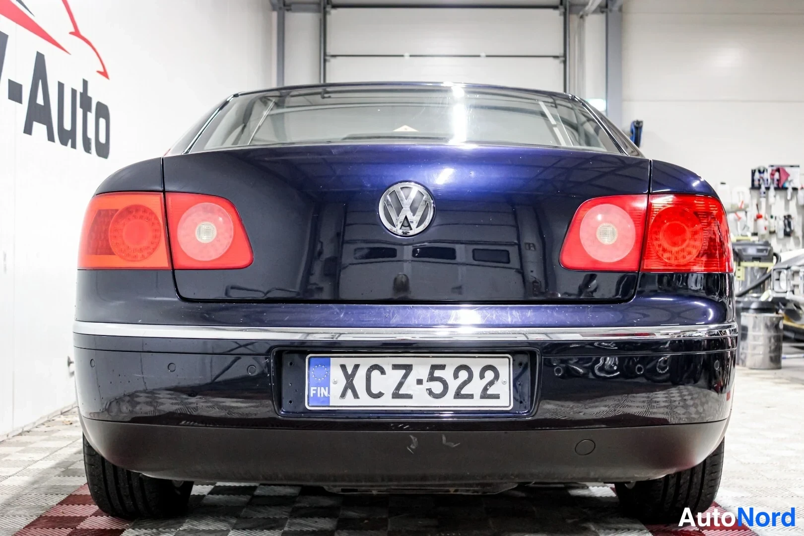 Takaa: Tummansinisen Volkswagen Phaetonin takaosa suoraan edestä, VW-merkki ja rekisterikilpi.