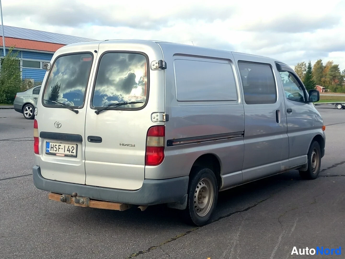 Takaviisto: Toyota Hiace -pakettiauto takaviistosta, hopeisenä; rekisterikilpi ja Hiace-merkintä takaluukussa.