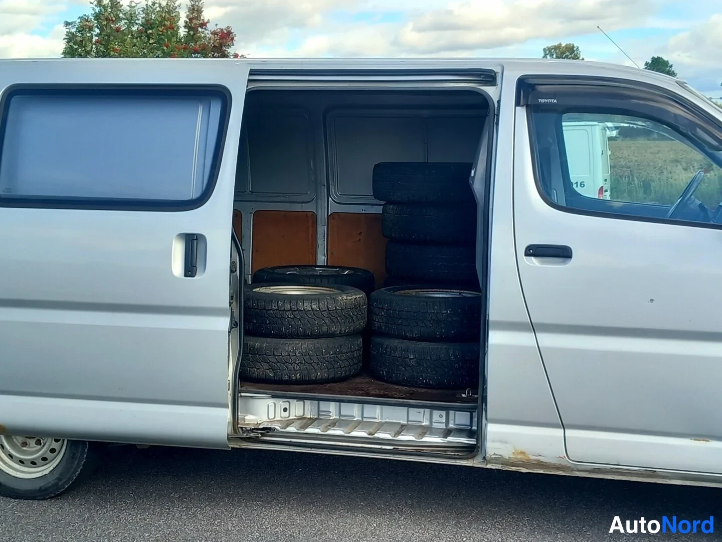Sivulta: Toyota Hiace -pakettiauto sivulta, liukuovi auki ja lataustilassa pinossa autonrengassarja.