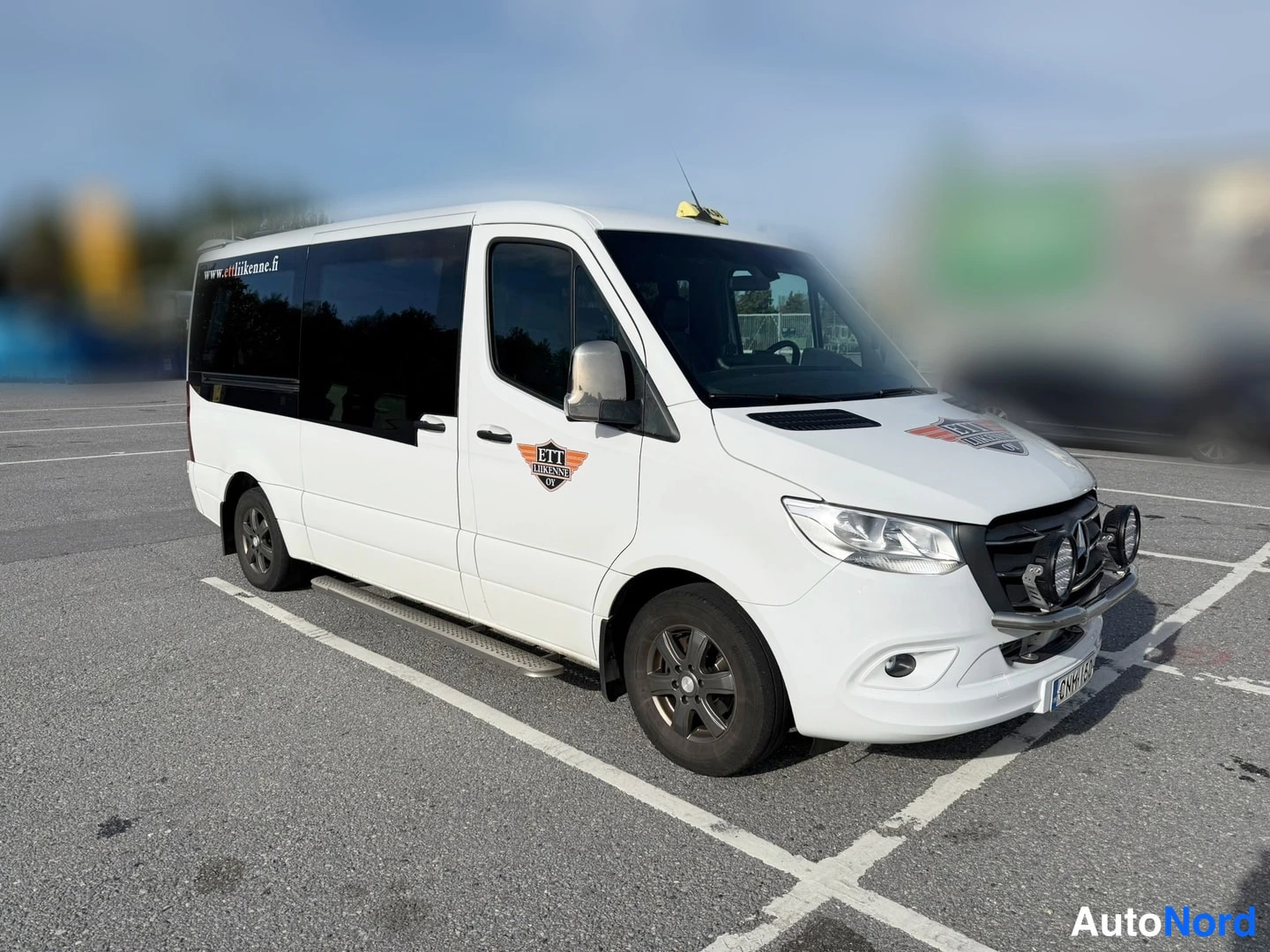 Etuviisto, nokka oikealle: Valkoinen Mercedes-Benz Sprinter -pakettiauto kuvattu kolmannelta etuviistöltä tullialueen parkkipaikalla.