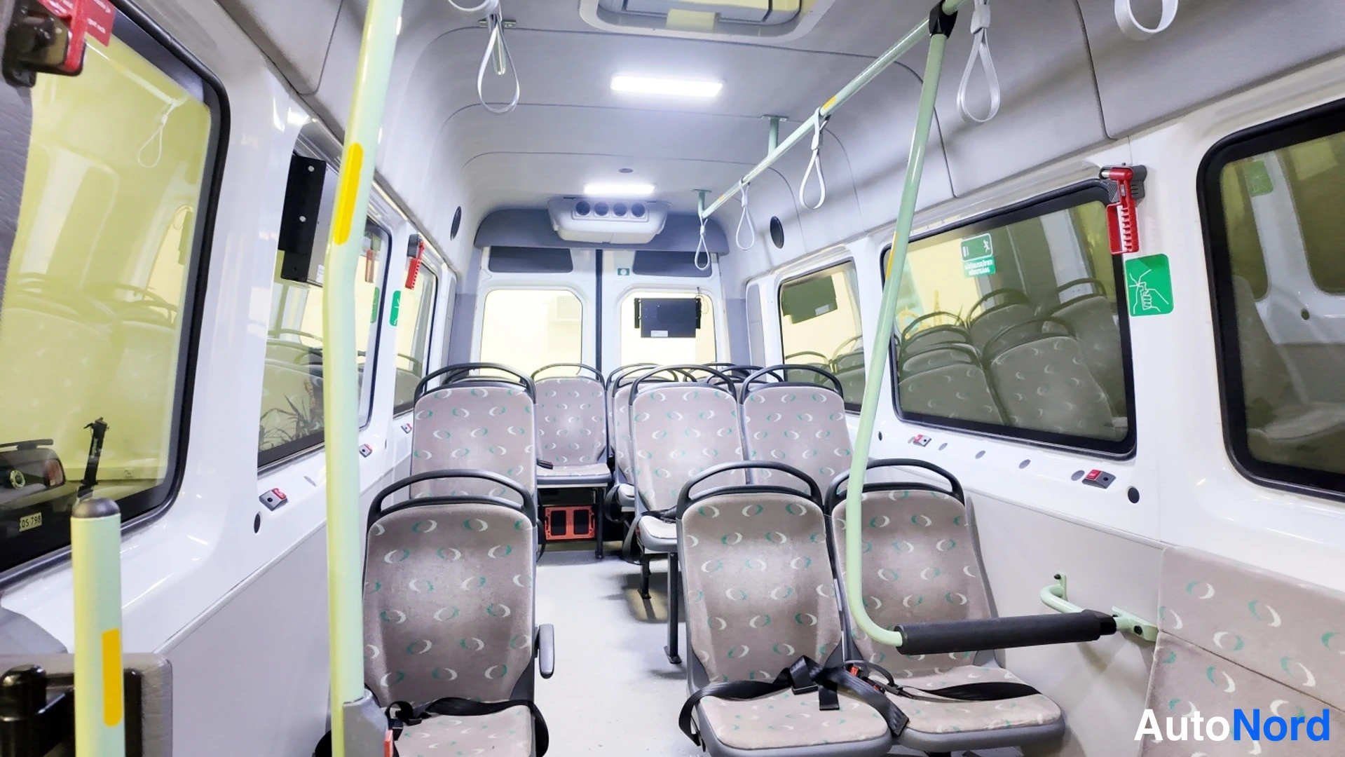 Muu: Pakettibussin sisätilat taakse päin kuvattuna: rivissä istuimia, keltaiset turvavyöt ja katon kohoumat.