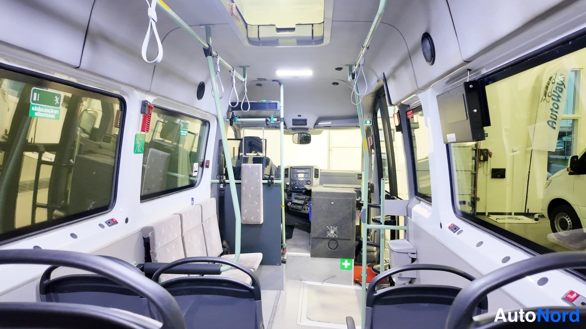 Muu: Pakettibussin sisätilojen kuvaa ääripäähän: penkkirivit, kuljettajan tilan laitepaneeli ja ikkunoiden näkymät ulos.