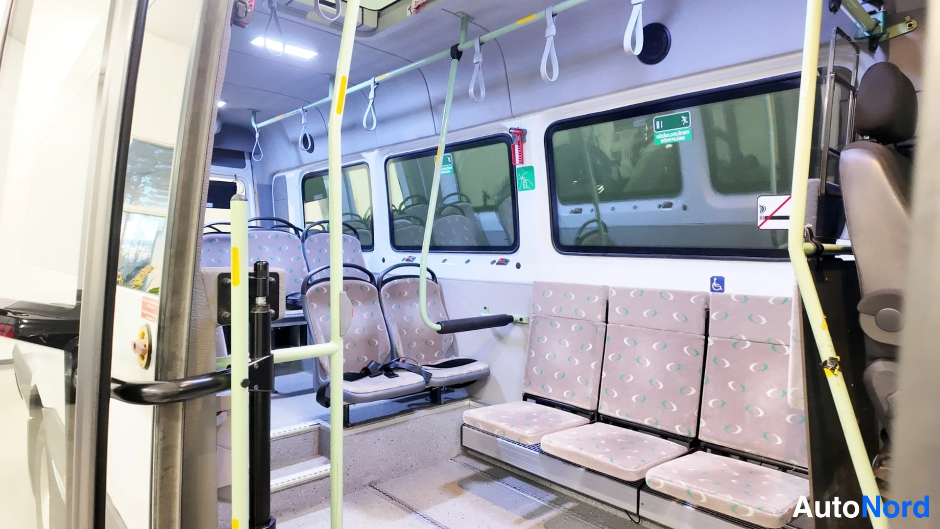 Muu: Pakettiauton muunnetun bussin sisätiloja: taittuva penkkirivi ja hoidinkahvat, kuva aukeavasta ovesta.