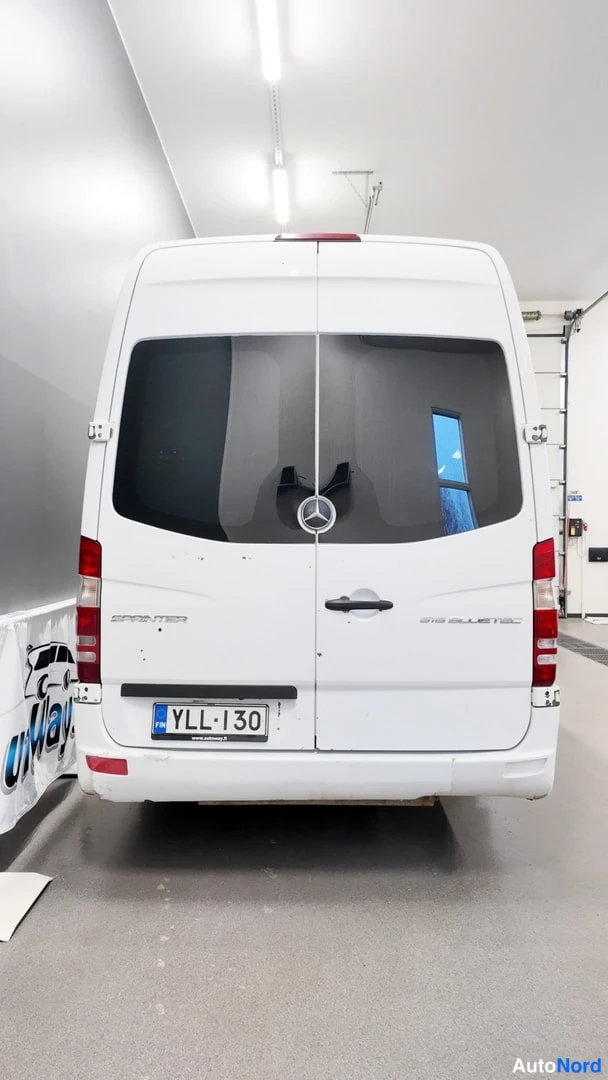 Takaa: Valkoisen Mercedes Sprinter -pakettiauton takaosa pysäköitynä autotallissa, rekisterikilpi.