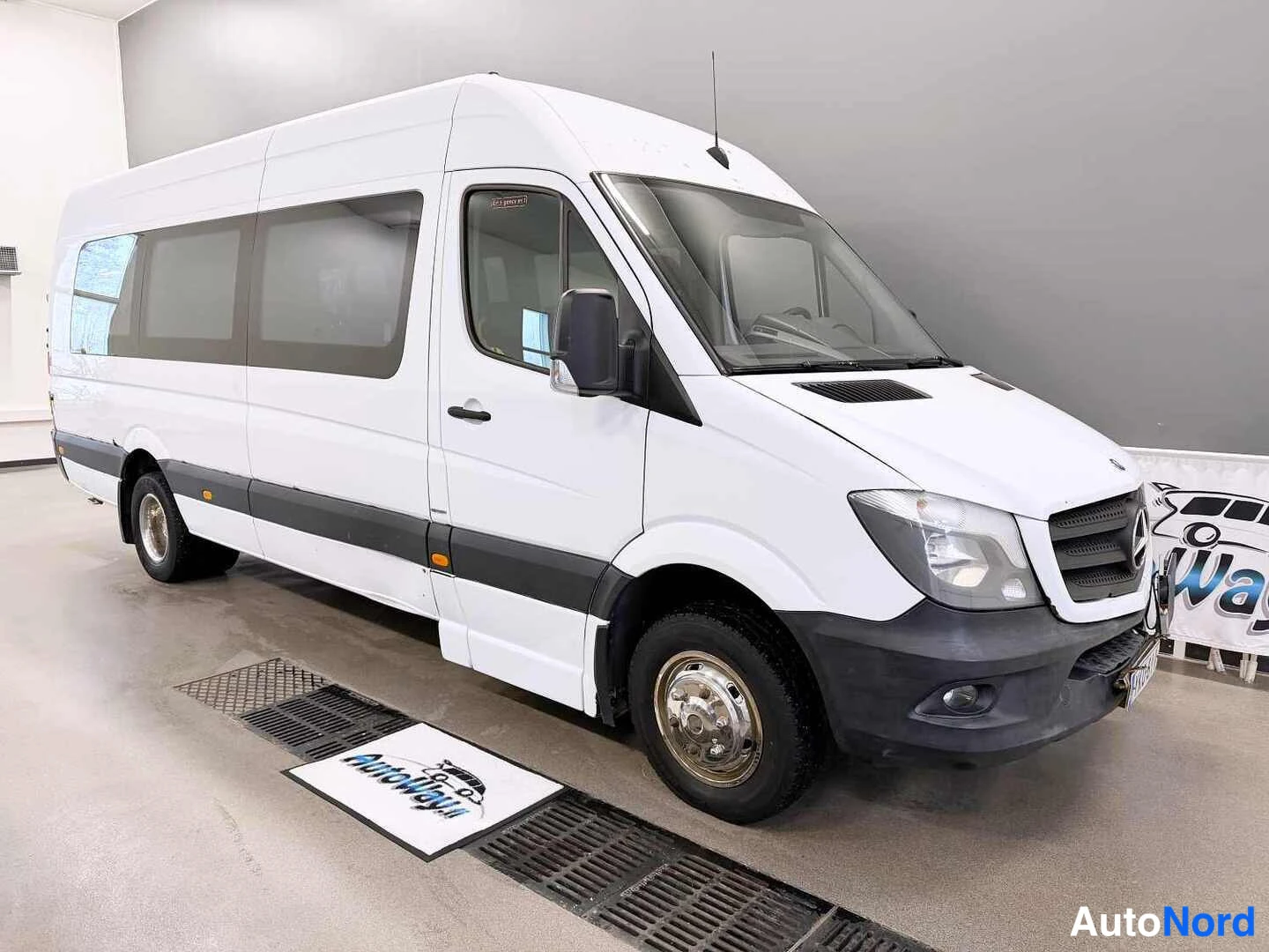 Etuviisto, nokka oikealle: Valkoinen Mercedes-Benz Sprinter -pakettiauto sisätiloissa etukulmasta vasemmalle asti näkyvän kyljen kanssa.