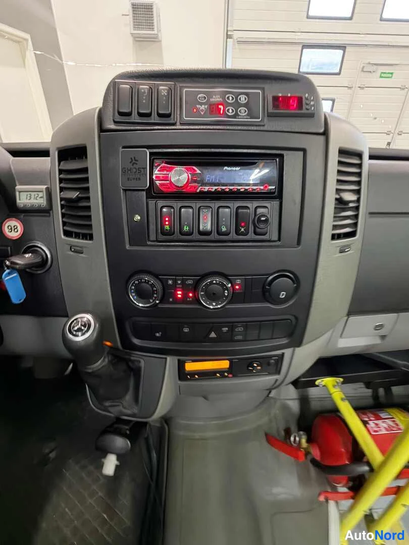 Takaa: Mercedes-Benz Sprinterin keskiöconsole lähikuvassa: Pioneer-radio, kytkinpaneelit, kiertonappiset lämpö- ja tuuletuksenhallinnat, vaihtajan keppi ja palosammuti