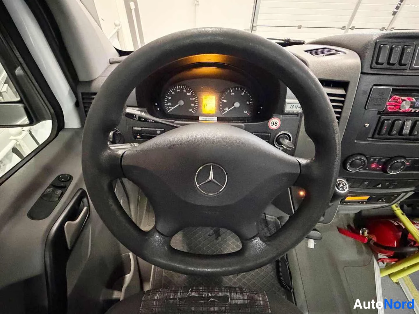 Edestä: Mercedes-Benz Sprinterin ratti ja mittaristo: Mercedes-tähti ratissa, taustavalaistut mittarit ja kojelaudan näyttö.