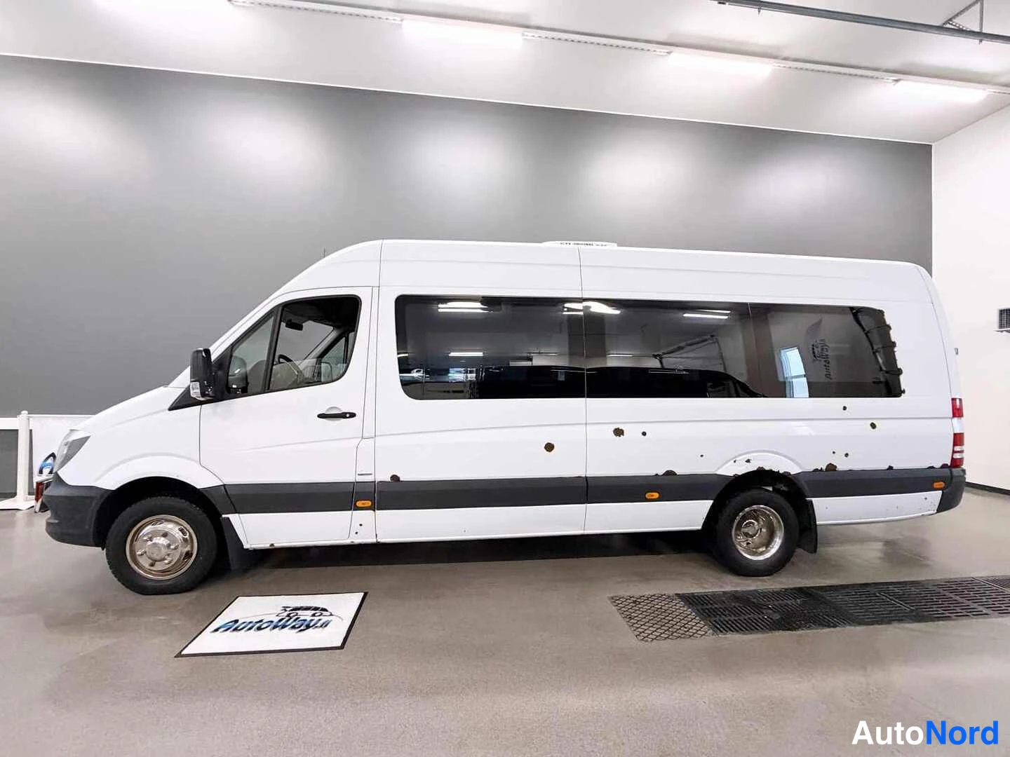 Sivulta: Sivukuvassa valkoinen Mercedes-Benz Sprinter -pakettiauto sisähallissa.