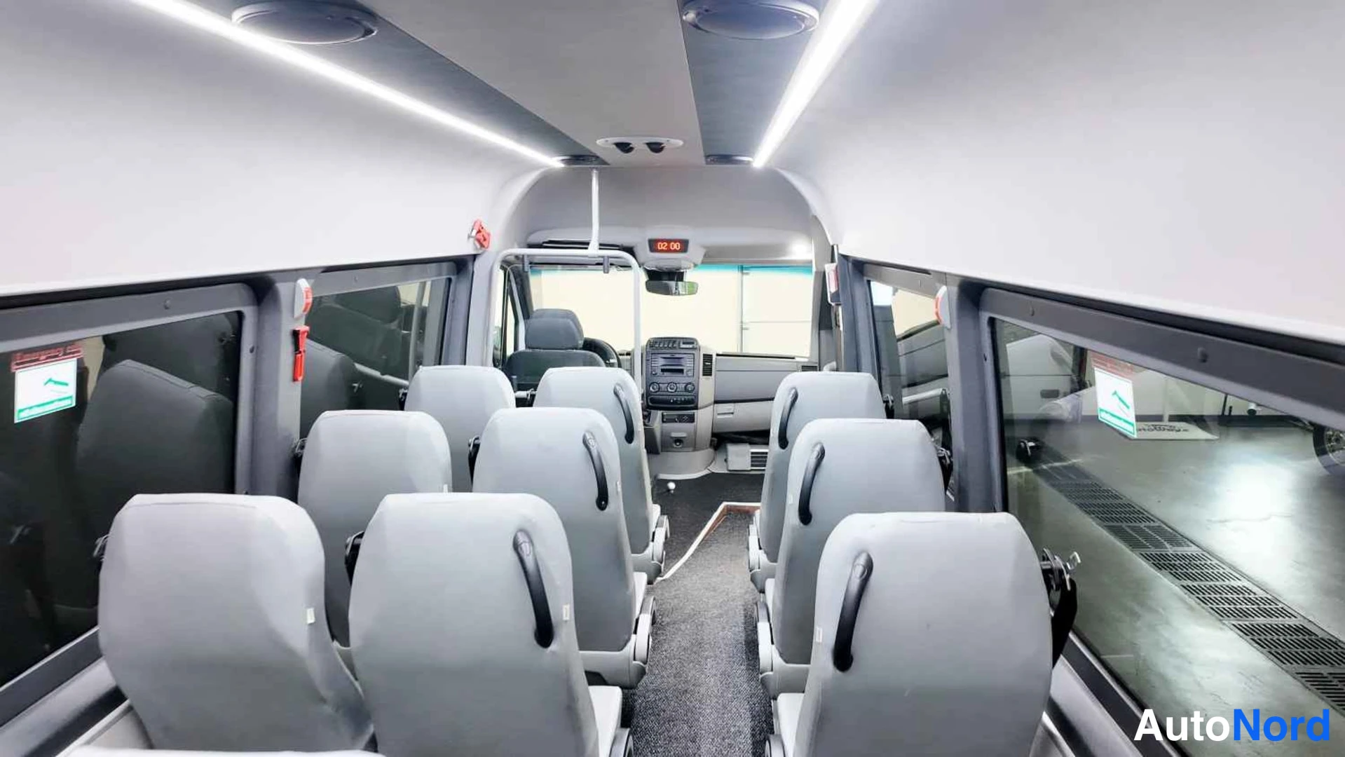 Muu: Minibussin sisätilat: kaksi istuinriviä tummia yksittäisiä istuimia kohti eteenpäin, kevyt sisävalaistus ja pieni kuljettajan osa.