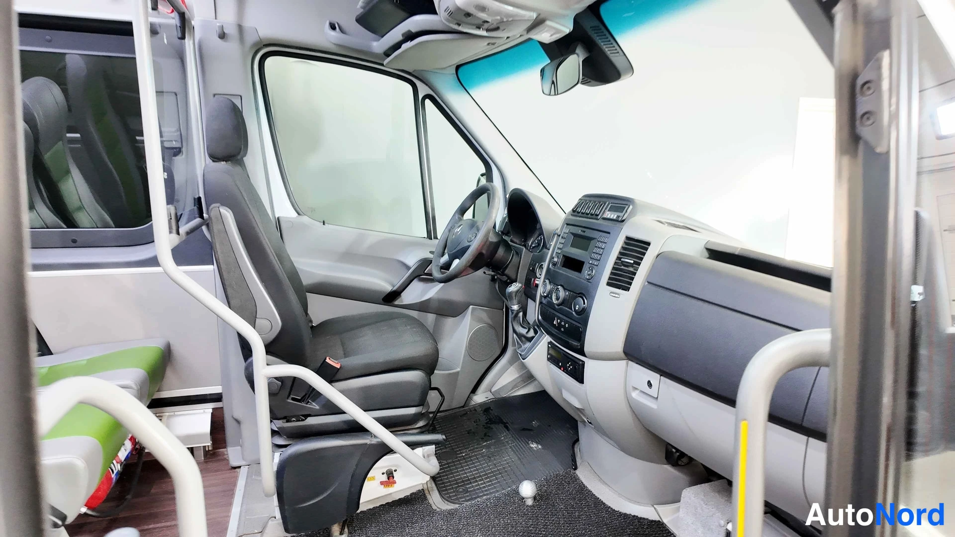 Sivulta: Mercedes-Benz Sprinterin ohjaamo kuvattuna oven puolelta: ohjauspyörä, kojetaulu ja penkit näkyvät.