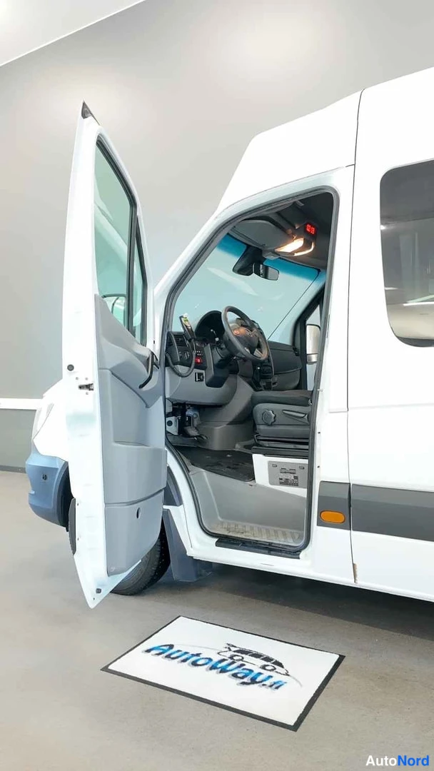 Sivulta: Valkoisen pakettiauton kuljettajan ovi auki, näkyvissä ohjaamo, ohjauspyörä ja kaatoistuin Autowayn lattiamaton päällä.