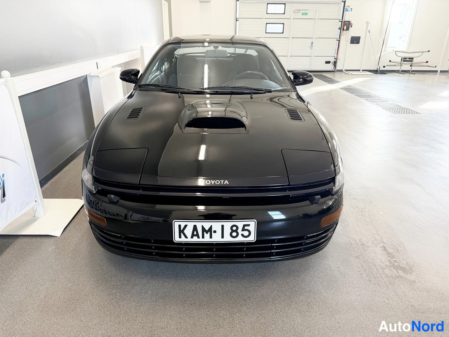 Edestä: Musta Toyota Celica edestäpäin kuvattuna rekisterikilpi näkyvissä.