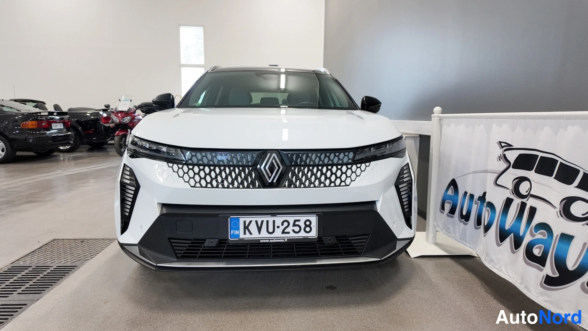 Edestä: Renault Scenic, etunäkymä, valkoinen kori ja musta promoottori, rekisterikilpi.