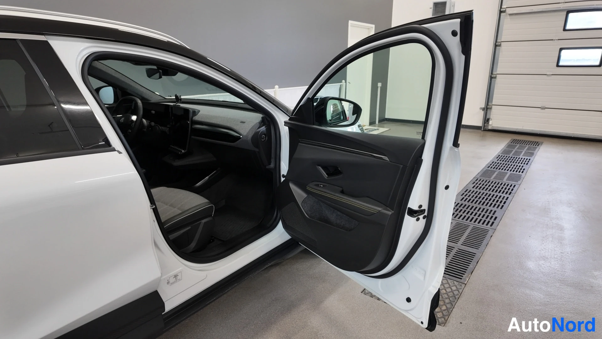 Sivulta: Auton kuljettajan puolen ovi auki, näkyvät auton etuistuin ja oven sisäpaneeli valkoisessa autossa.