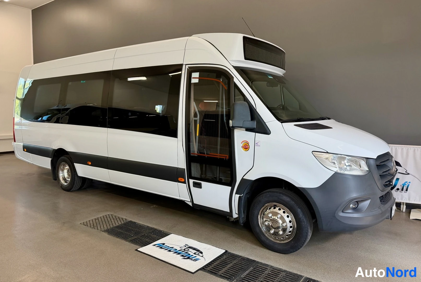 Etuviisto, nokka oikealle: Valkoinen Mercedes-Benz Sprinter -tilausajoneuvo nähtynä kolmivartalo-otoksessa keula oikealla, etuovi auki sisätiloihin.