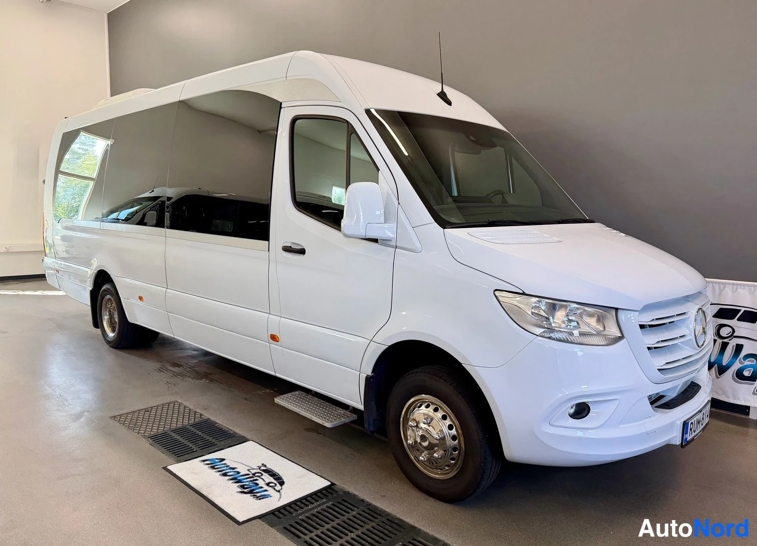 Etuviisto, nokka oikealle: Mercedes-Benz Sprinter -pakettiauto valkoisena etukulmasta sisätilassa, keula ja vasen kylki näkyvissä.