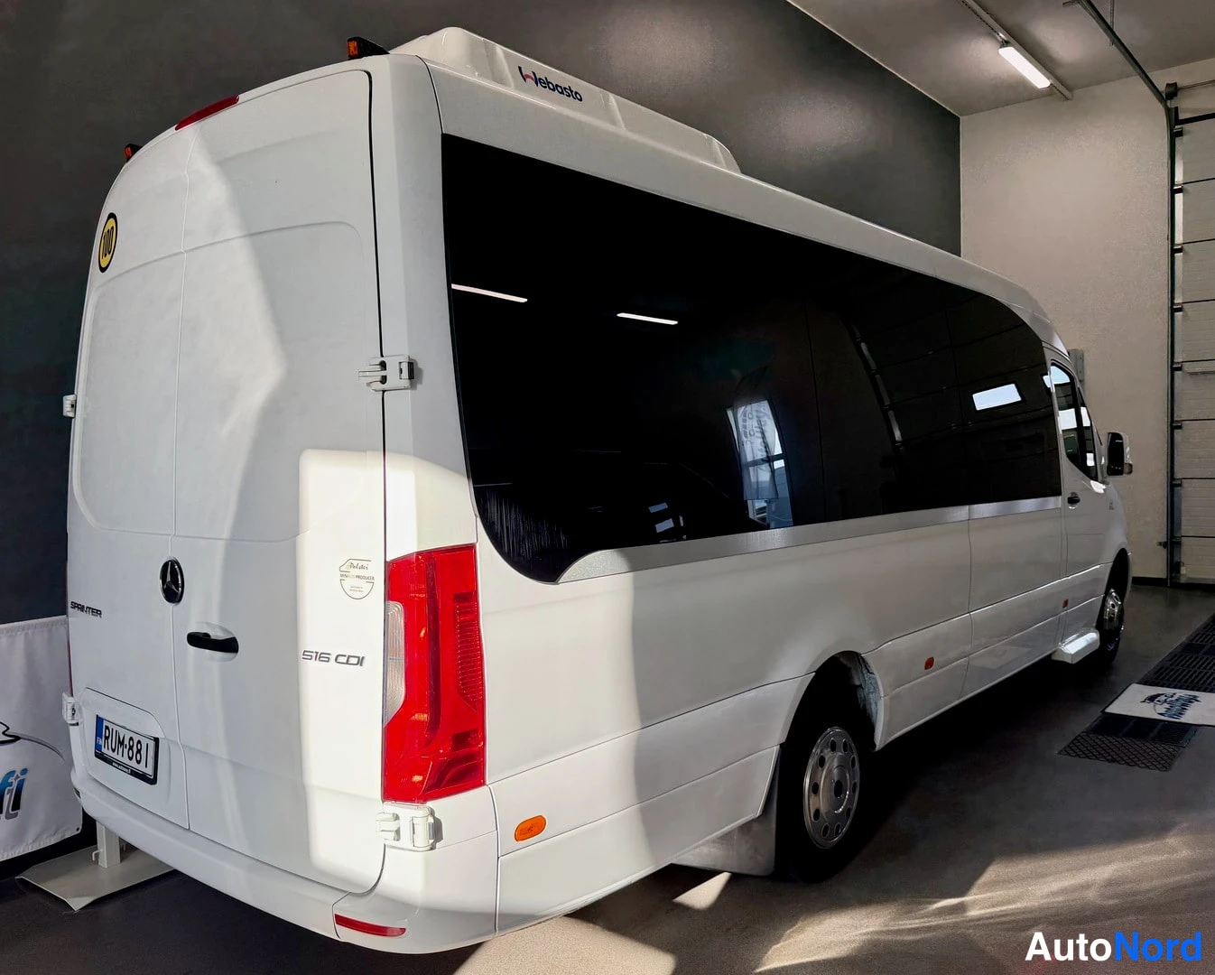 Takaviisto: Valkoisen Mercedes-Benz Sprinter -bussin takakulma vasemmalta: korin takaosaa ja pitkää sivua ikkunoineen sisätiloissa.