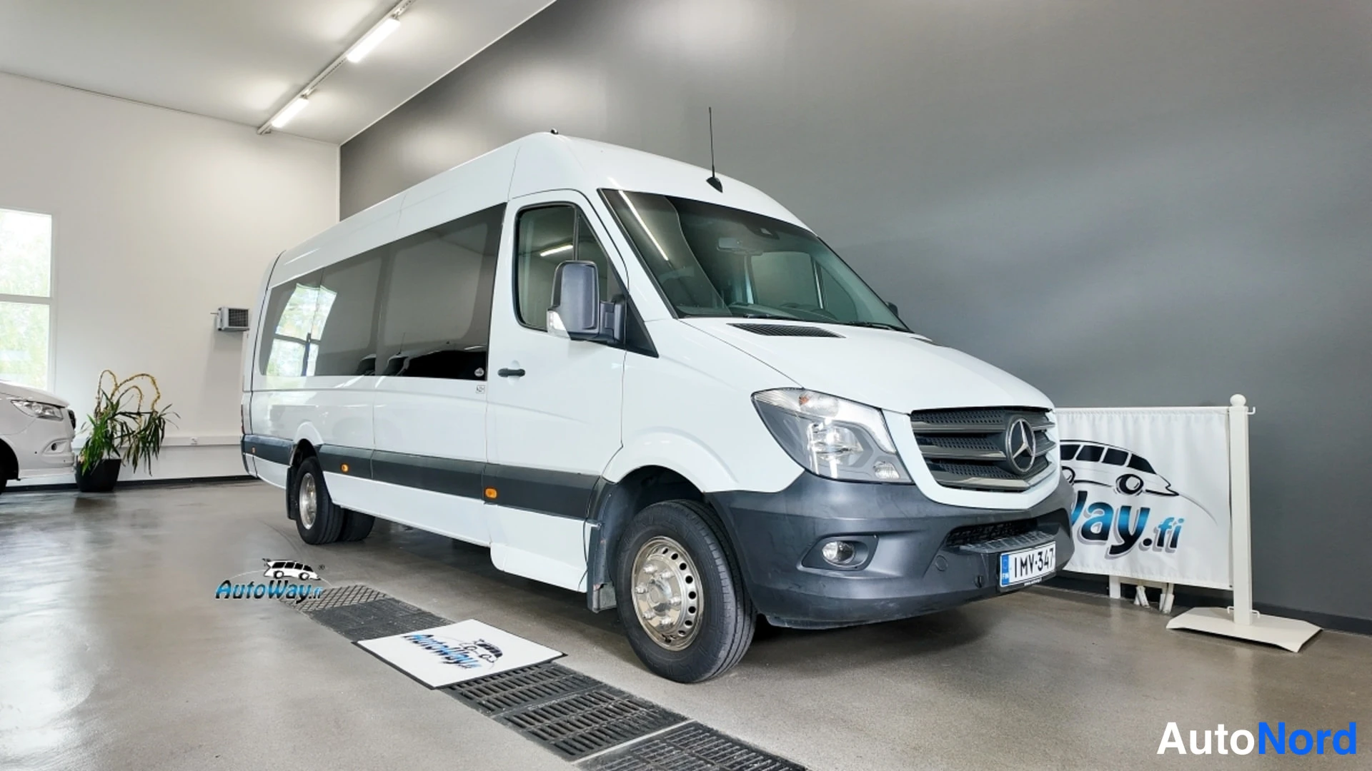 Etuviisto, nokka oikealle: Valkoinen Mercedes-Benz Sprinter -pakettiauto etukulmasta oikealta nähtynä sisätiloissa.