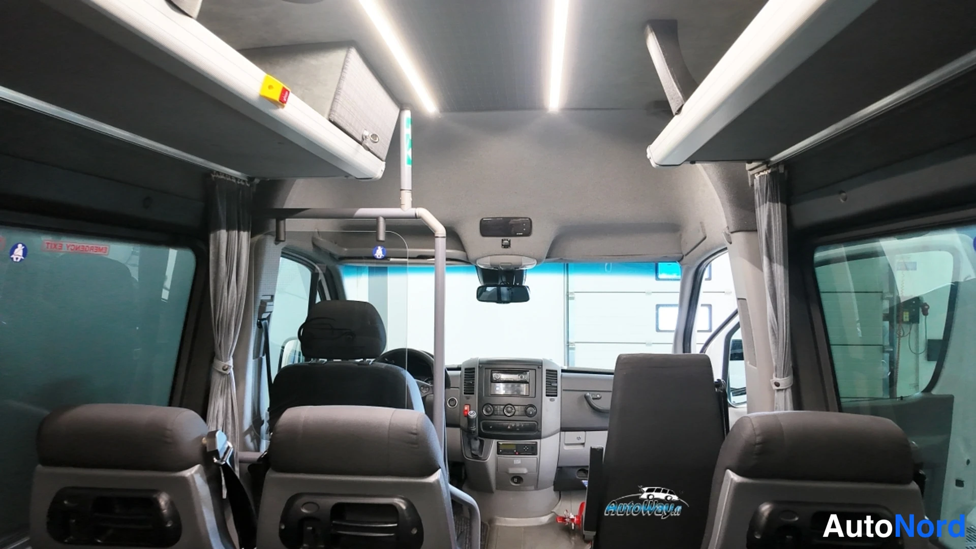 Muu: Pakettiautobussin sisätilat keulaan päin: etutuolit, kuljettajan ohjaamo kojelautoineen, oven yläkäsijoitin ja kattoluukku.