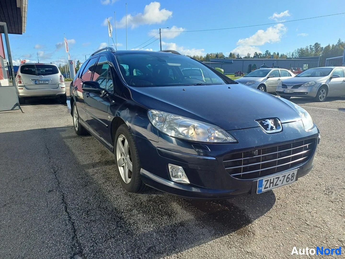 Etuviisto, nokka oikealle: Tummansininen Peugeot 407 SW -farmaria edestä viistosti kuvattuna; rekisterikilpi ja kromivanneet näkyvät.
