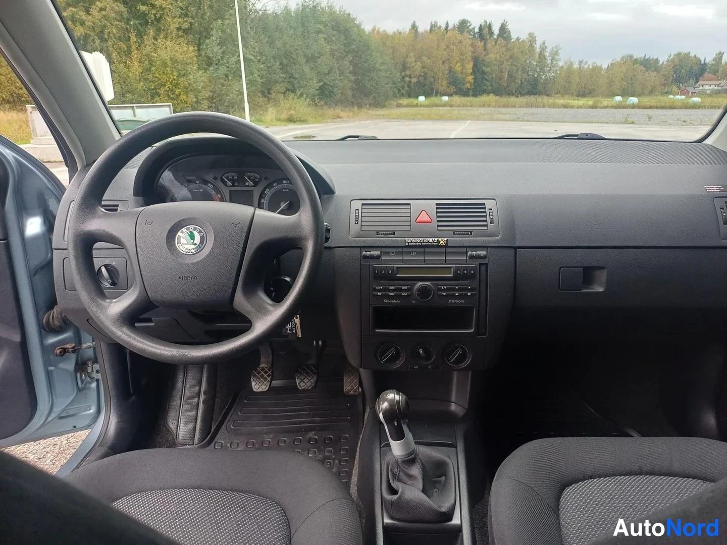 Muu: Näkymä auton kojelautaan ja tuulilasista eteenpäin: Skoda-ohjauspyörä, radio-ja lämpöpainesäädöt, manuaalivaihtokeksi.