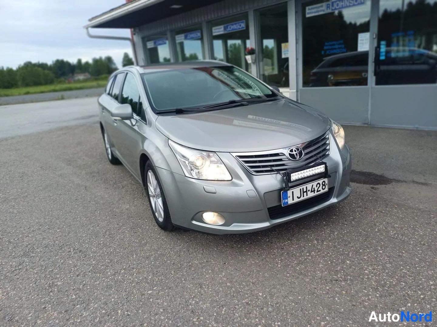 Etuviisto, nokka oikealle: Hopeanharmaa Toyota Avensis Farmari kulmittain edestä oikealta, rekisteritunnus I JH-428, etupuskurissa lisävalo.