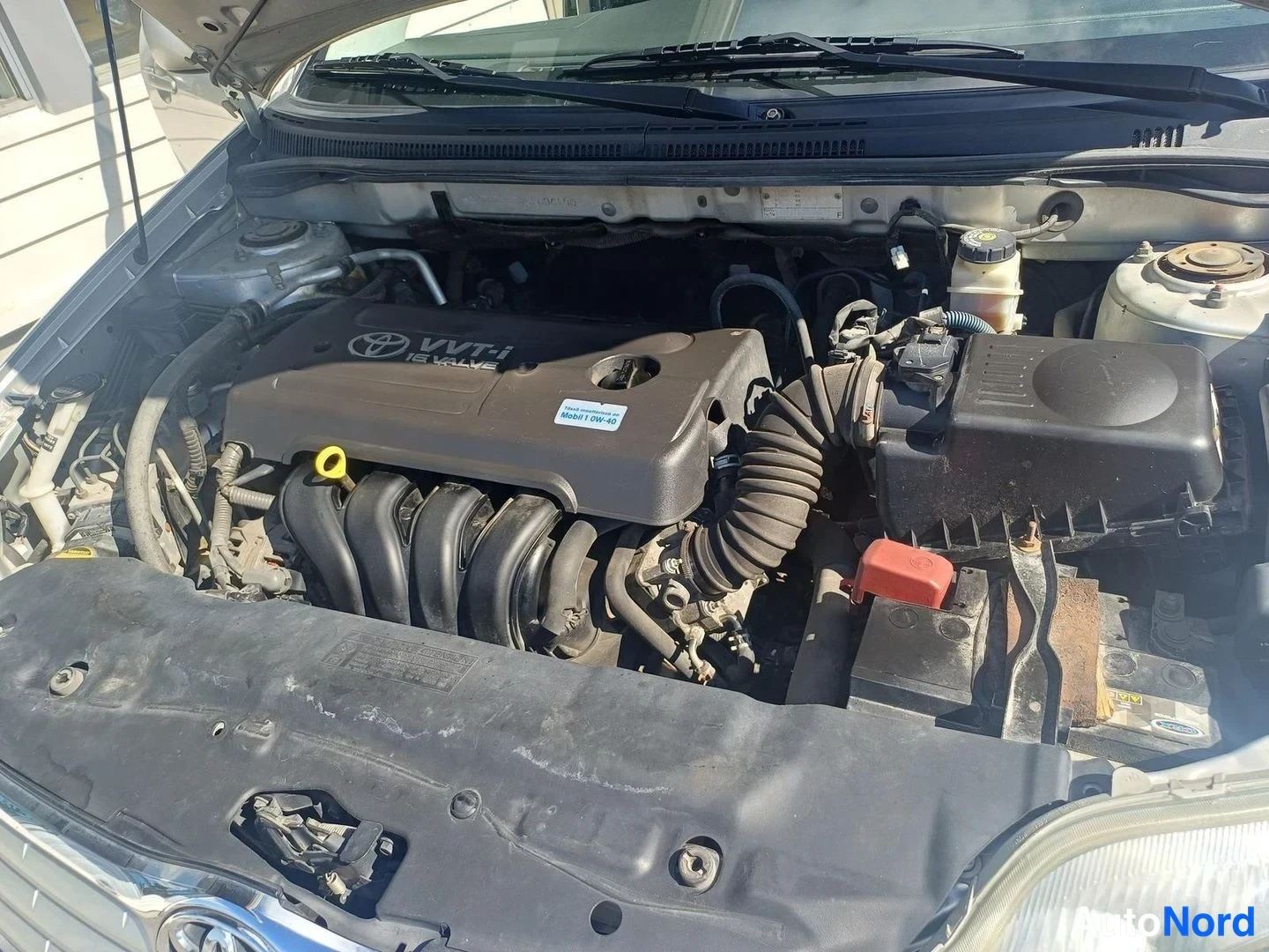 Muu: Moottoritila avattuna: Toyota VVT-i 16 VALVE -merkitty moottori, ilmansuodatinlaatikko, akku ja jäähdytinNesteen säiliö näkyvissä.