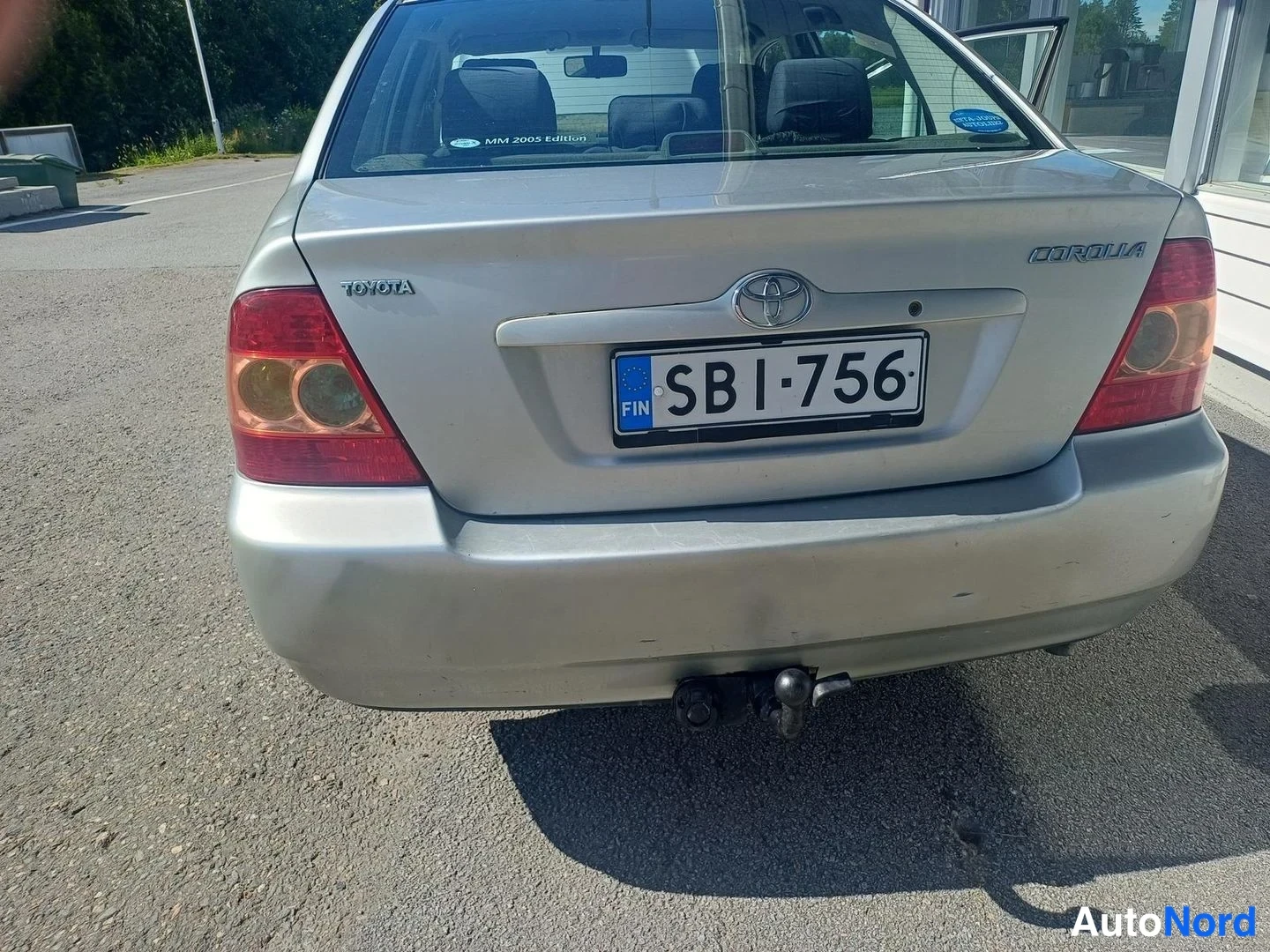 Takaa: Hopeanharmaan Toyota Corolla -sedanin takapää; rekisterikilpi FIN SB1-756 ja perävaunun kytkin takapuskurissa.