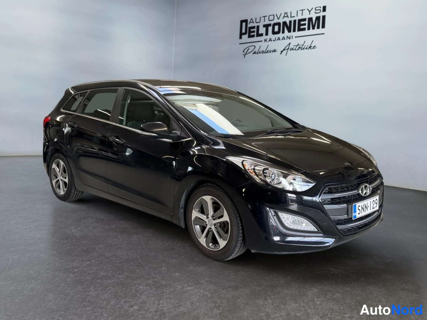 Etuviisto, nokka oikealle: Mustan farmariauton etukulmanäkyvyys, Hyundai-merkki ja rekisterikilpi näkyvissä.