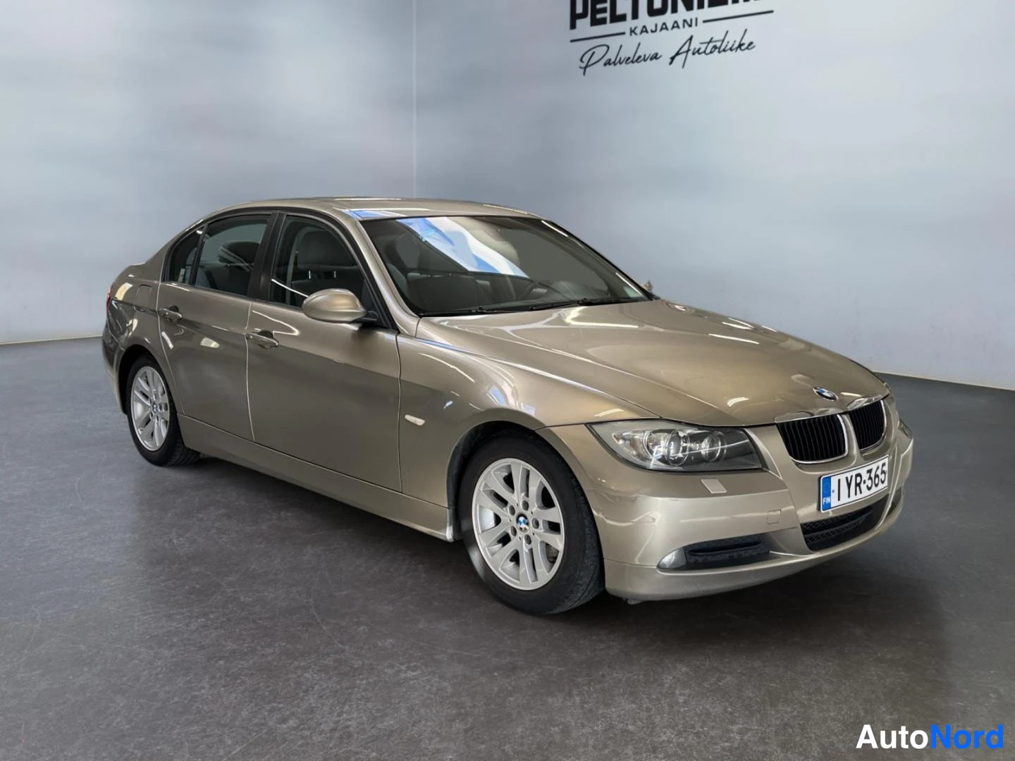 Etuviisto, nokka oikealle: BMW-sedanin etukulmaneva kuva vaalean kultasävyisenä, etusäleikö ja rekisterikilpi näkyvät hallitilassa.