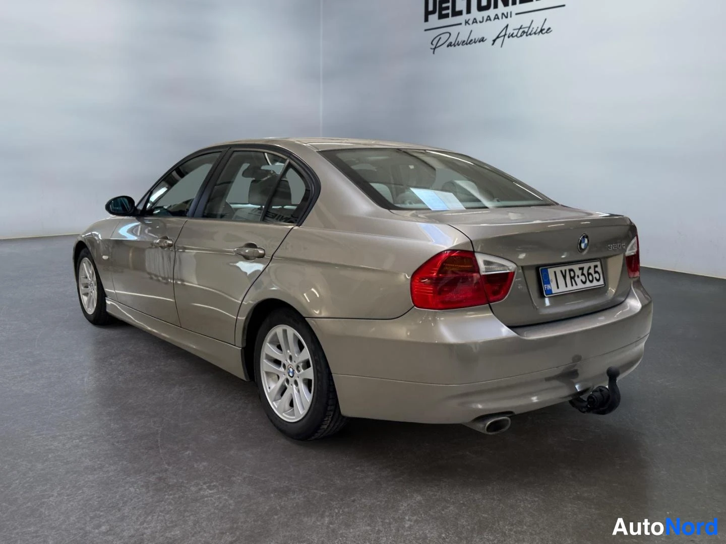 Takaviisto: BMW-sedan takakulma sisätiloissa, rekisteritunnus 1YR-365, beige metallinhohtoinen maalaus, kylki ja perä näkyvissä, vetokoulu takapuskurissa.