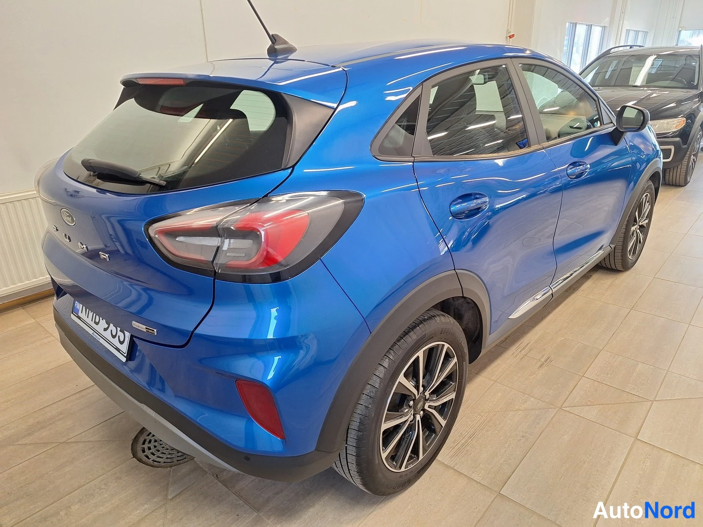 Takaviisto: Sininen Ford Puma takaosta ja oikeaa sivua kuvattuna autonäyttelytilassa, kilpi.