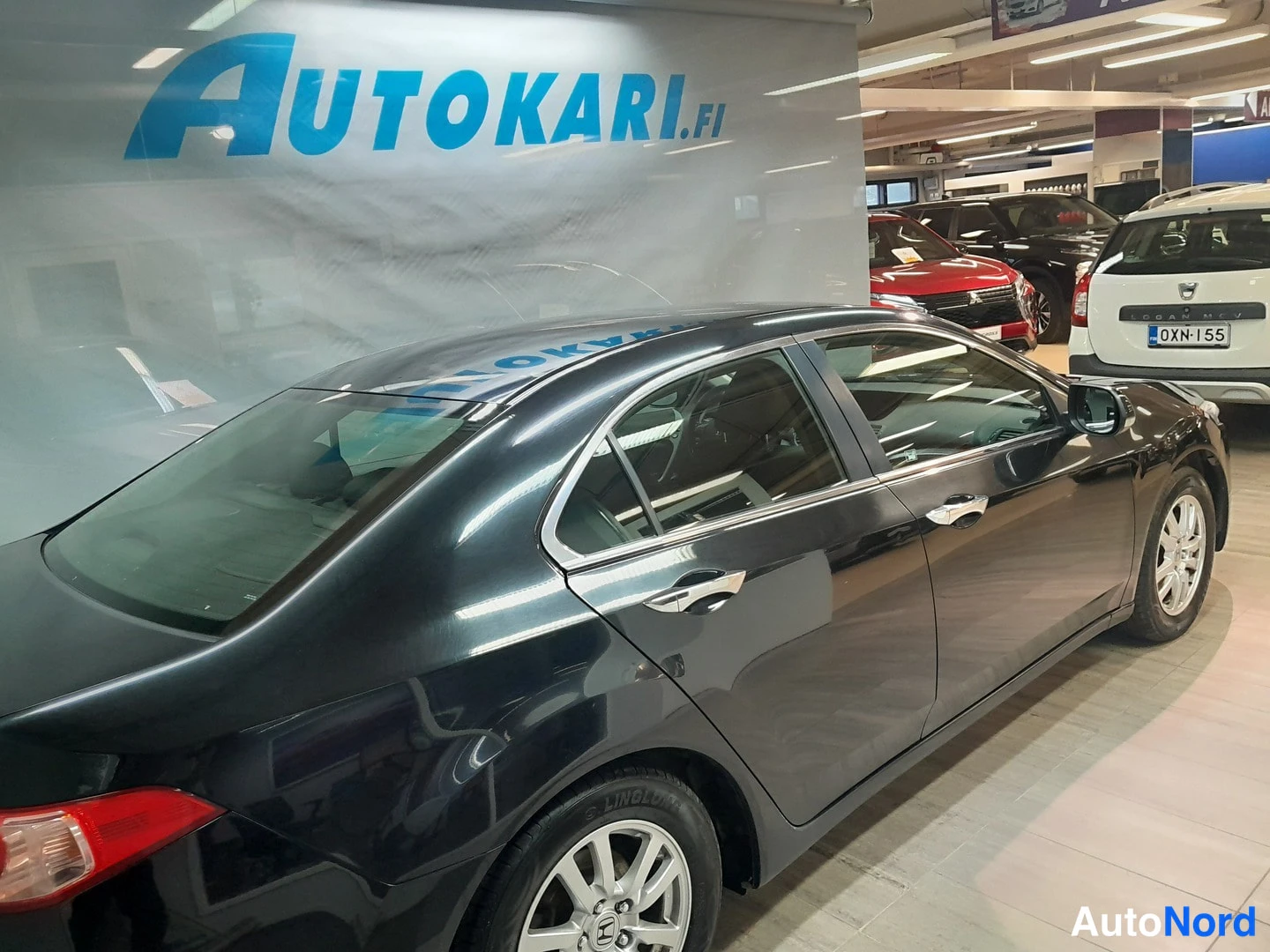 Takaviisto: Mustan Honda Accord -sedanin takapää ja oikea sivu kuvattuna sisätiloissa, taustalla muita autoja.