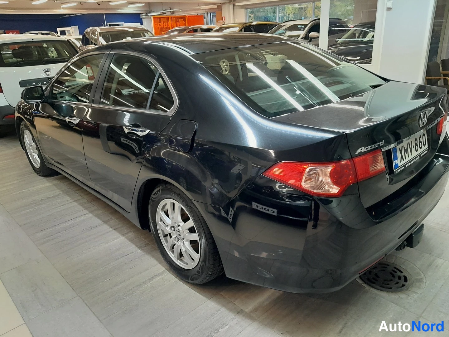 Takaviisto: Mustan Honda Accord -sedanin takakulma, lohkolämmitintulppa ja rekisterikilpi näkyvät, autonhallissa.