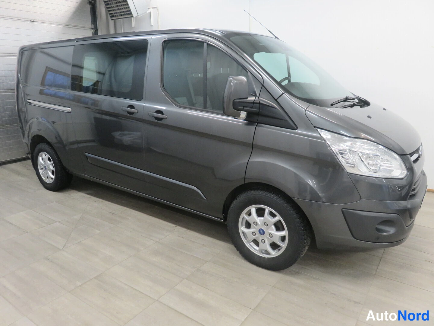 Etuviisto, nokka oikealle: Ford Transit Custom -pakettiauton etukulmanäkymä oikealta, auton koko runko näkyvissä tummanharmaana sisätiloissa.