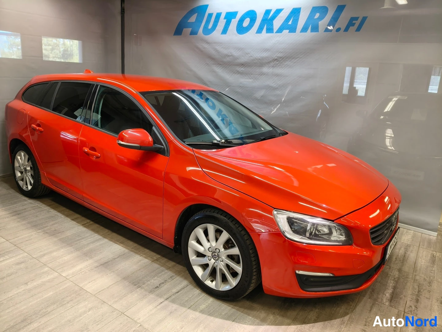 Etuviisto, nokka oikealle: Volvo V60 -farmari punaisena sisätiloissa, etukulma vasemmalta, keulalla ja kylki näkyvissä.